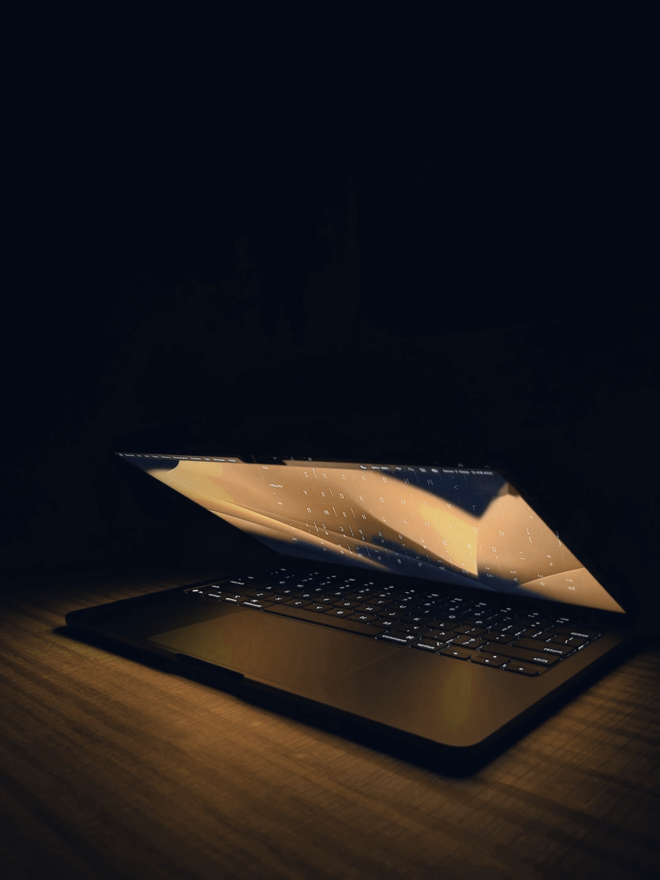 A half-open laptop glowing on a wooden table in a dark room.