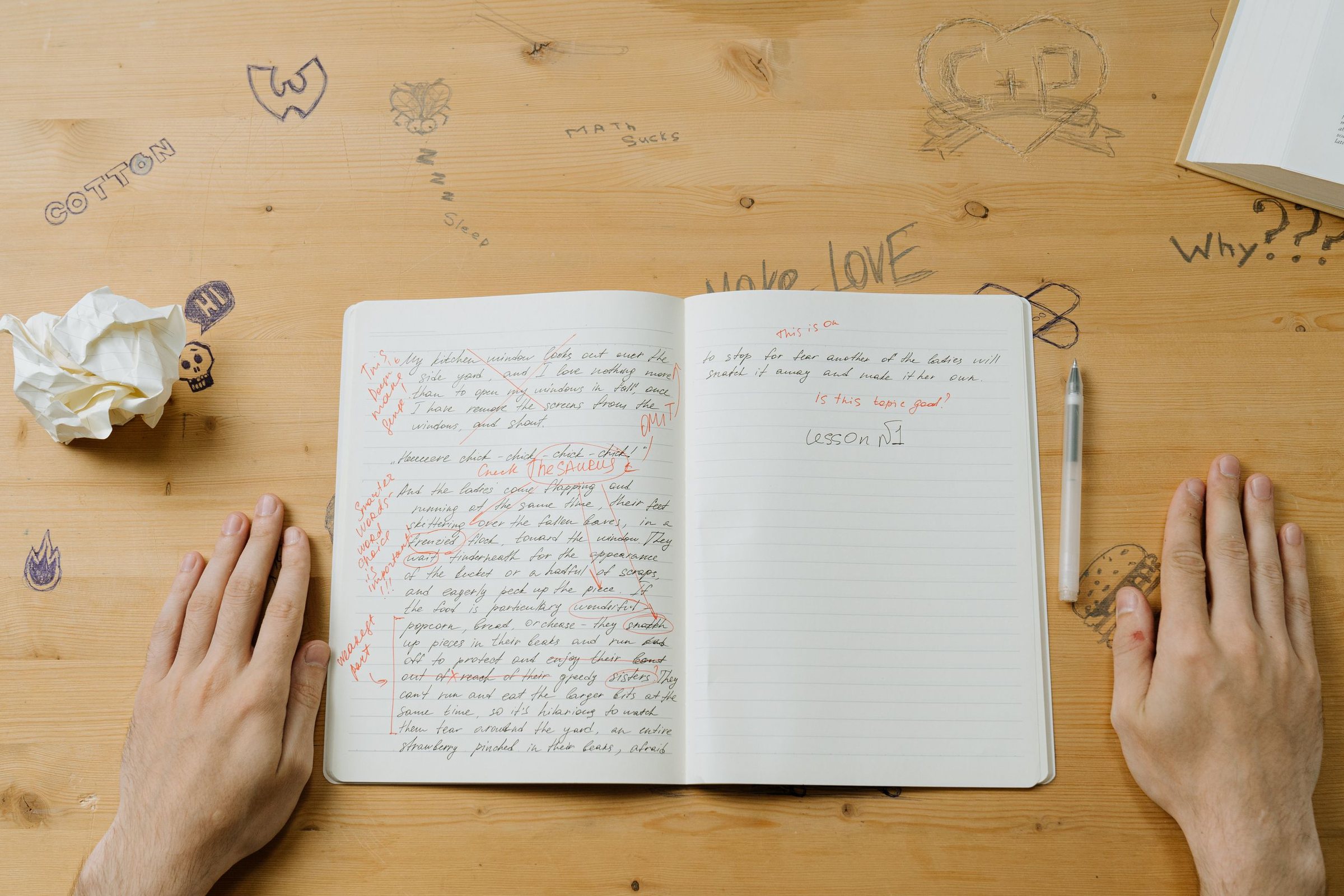 Hands either side of an open notebook of handwritten notes on a wooden desk.