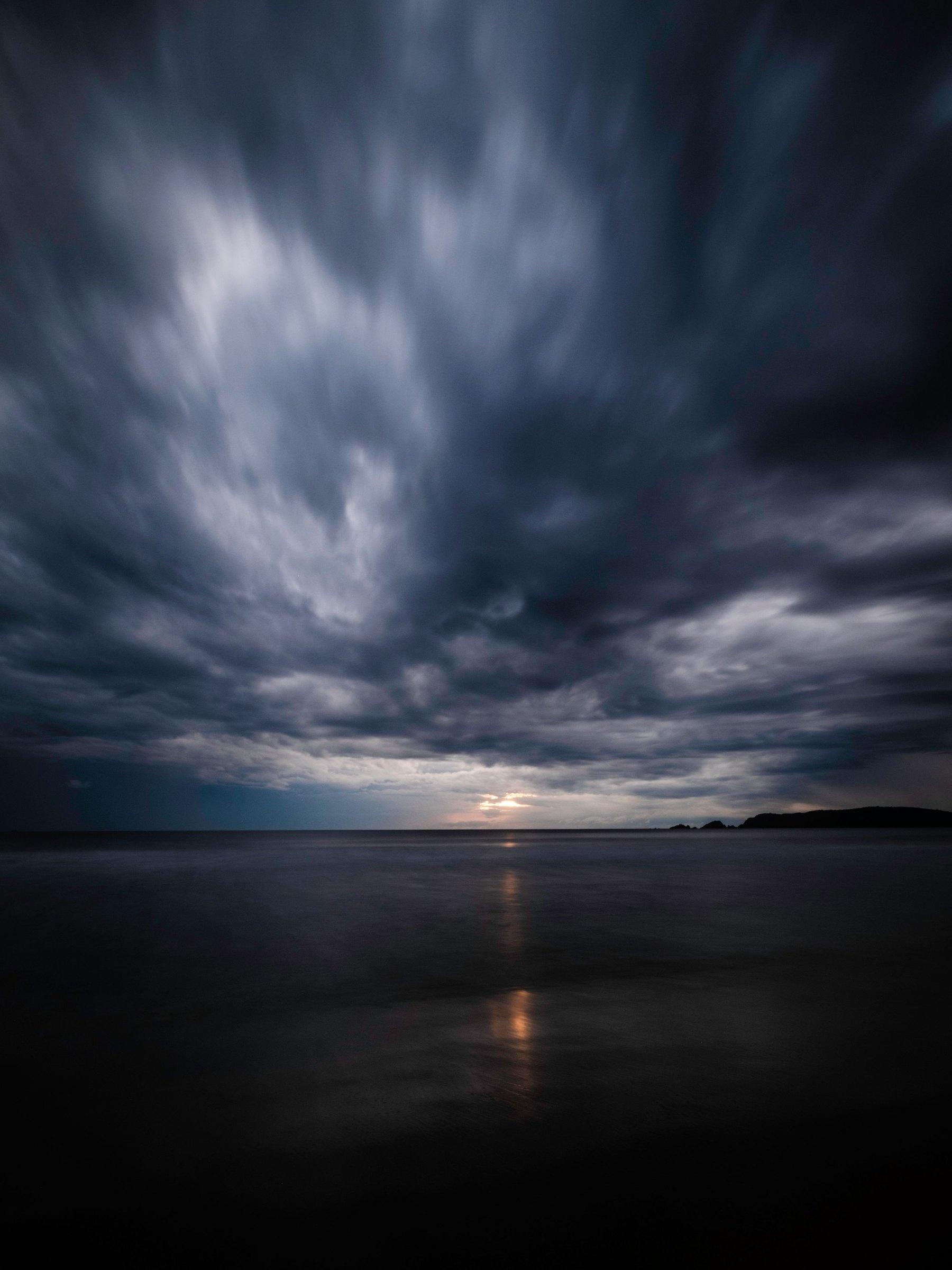Storm clouds rolling in over a dark, calm sea.