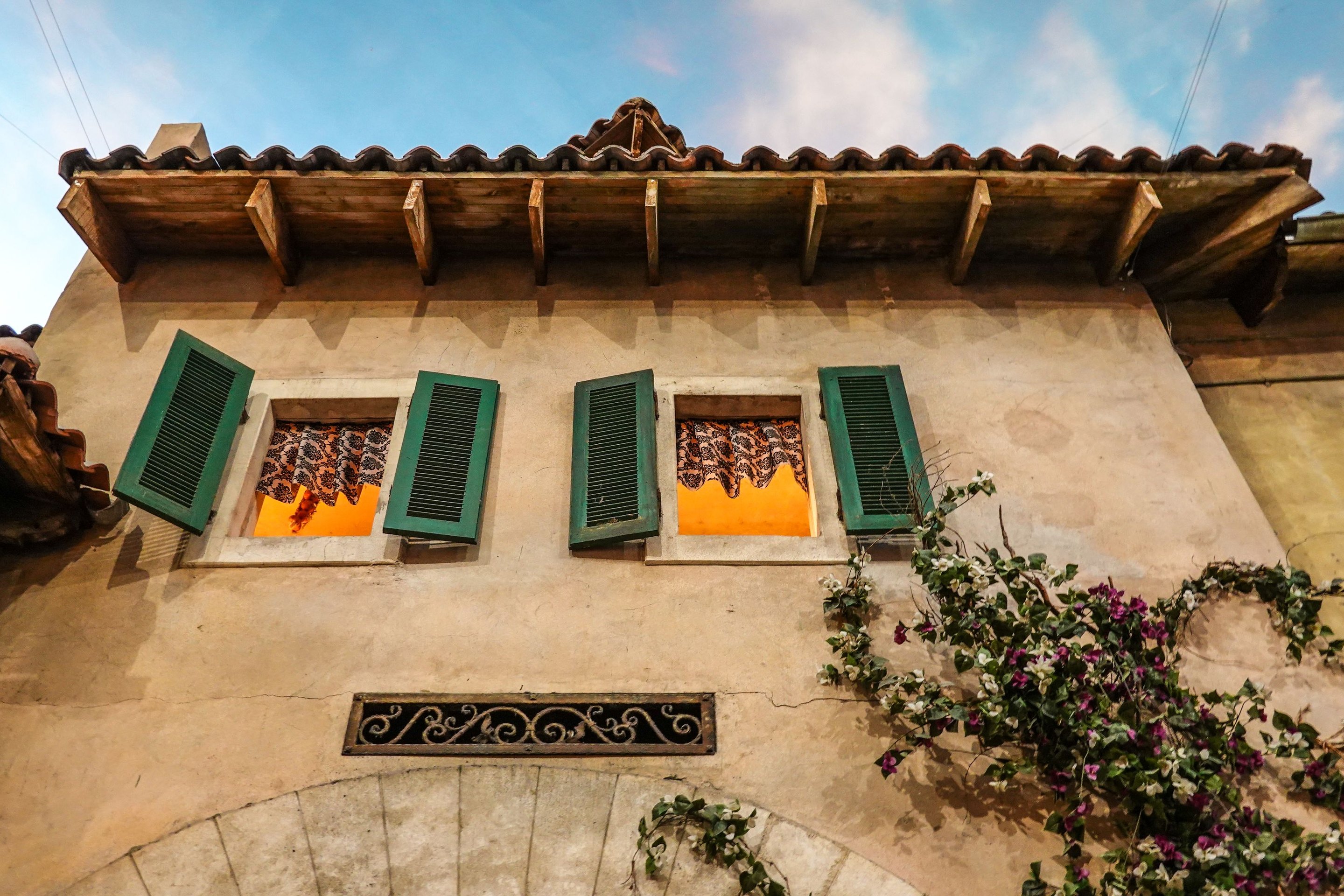 An old house facade with green wooden shutters and warm light in the windows.