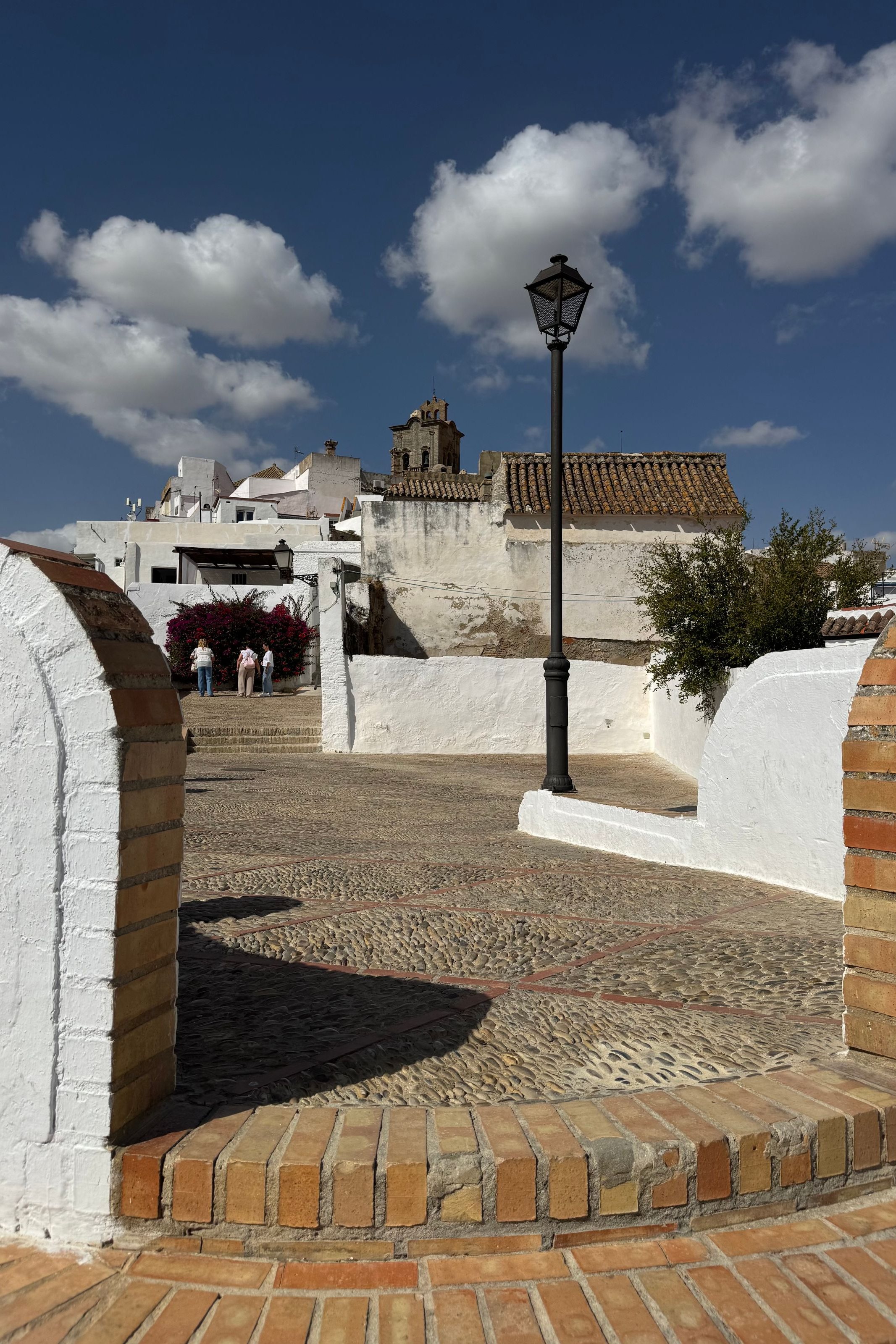 A whitewashed village corner in Spain: lime-white walls, brick edging and cobbles in deep afternoon shade.
