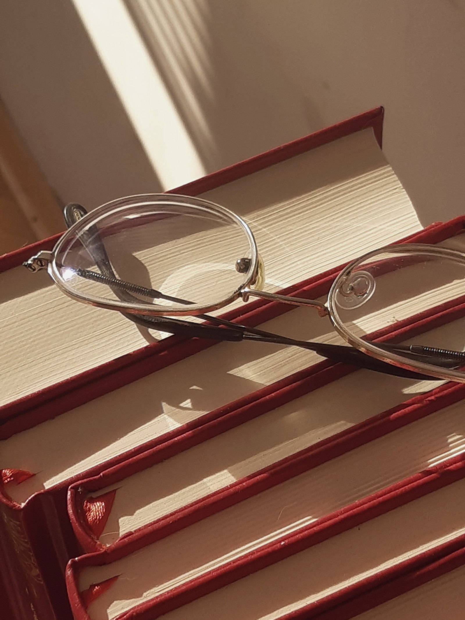 Reading glasses resting on a stack of hardback books in late afternoon sun.