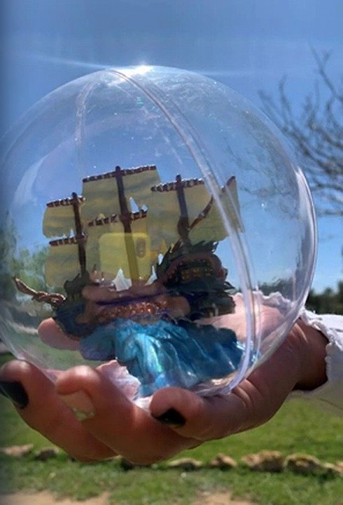 A figurine from Impressive Secret, inside a clear capsule, held in a hand.
