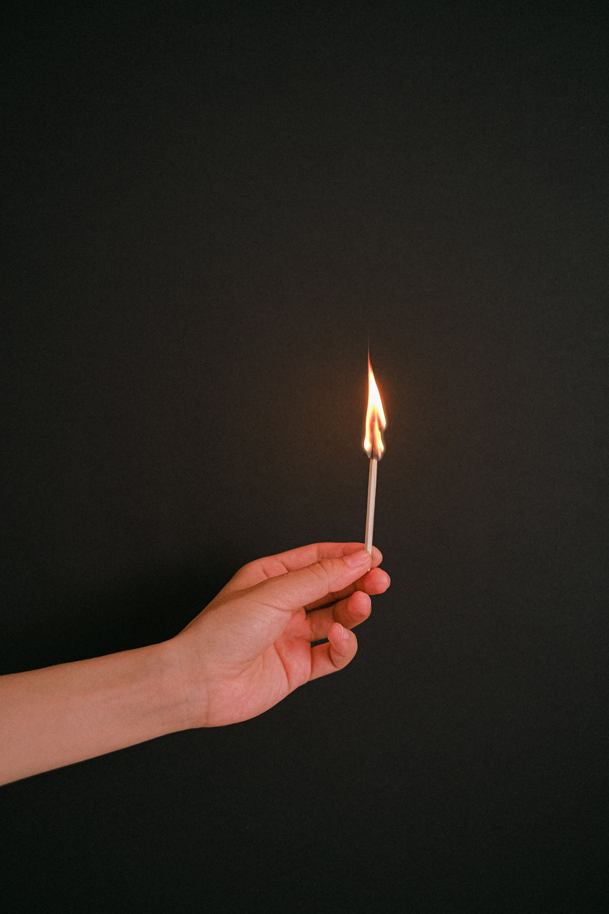 A hand holding a lit match against a dark background.