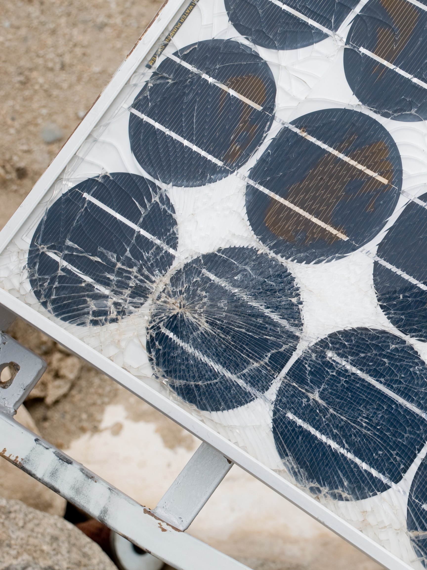 Close-up of a broken solar panel: shattered glass over round cells, frame bent at the corner.
