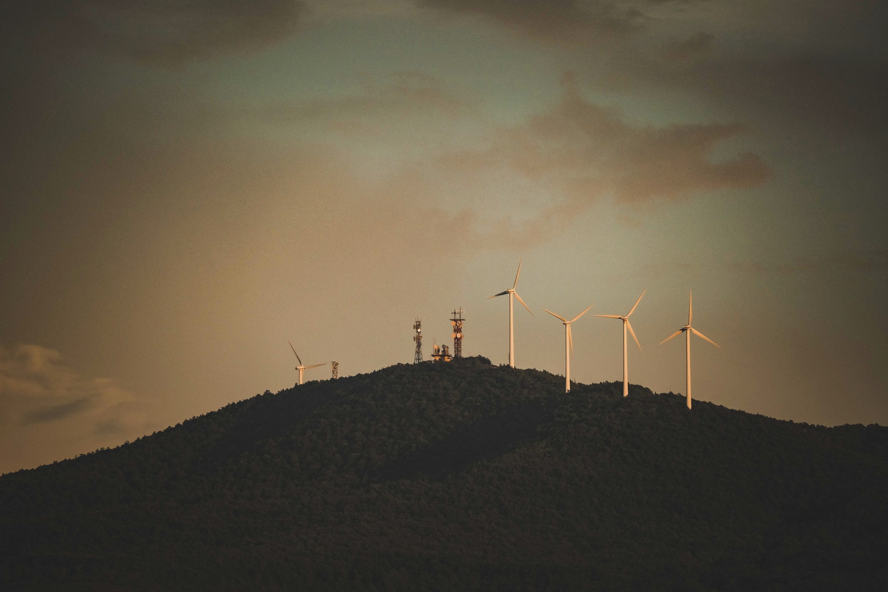 Wind turbines along a forested hill ridge at dusk
